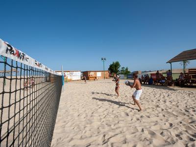 Zwei Personen spielen Beachvolleyball auf einem Sandplatz bei sonnigem Wetter.