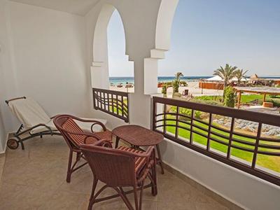 Balcon avec chaises et chaise longue surplombant le jardin et la mer sous un ciel bleu.