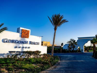 Eingangsschild von Gorgonia Beach mit Palmen und klarem blauem Himmel.