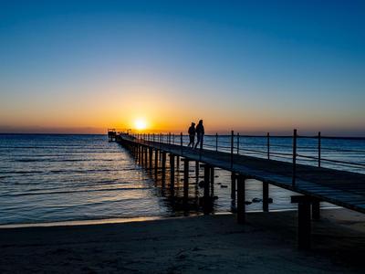 Steg am Strand bei Sonnenuntergang mit zwei Personen darauf