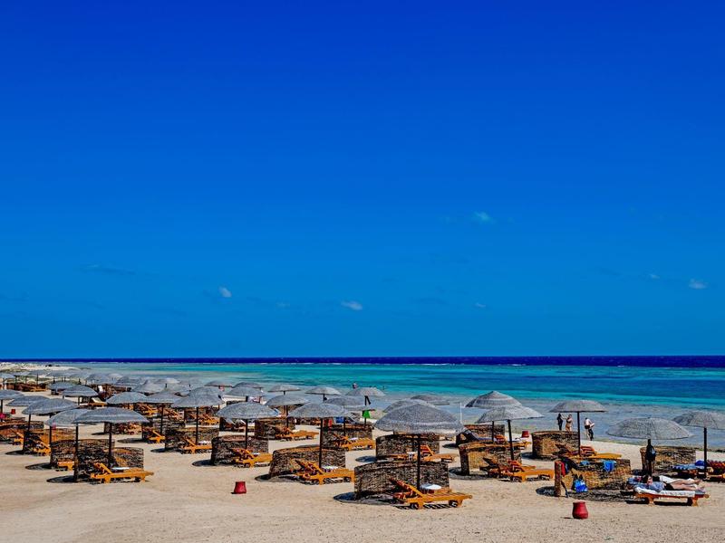 Rangée de transats avec parasols sur la plage sous un ciel bleu clair.