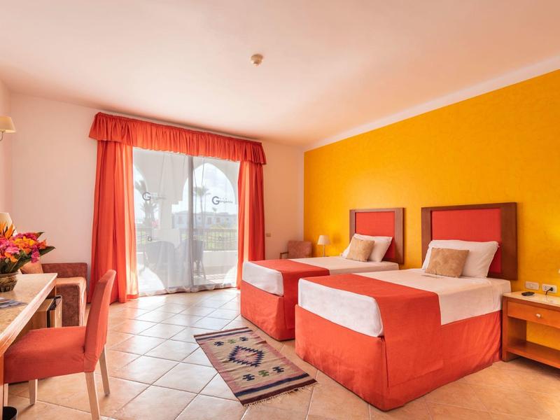 Chambre d'hôtel lumineuse avec deux lits simples et balcon donnant sur la piscine.