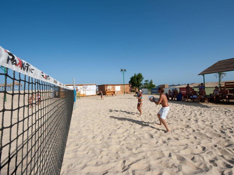 Deux personnes jouent au beach-volley sur du sable sous un ciel bleu clair.