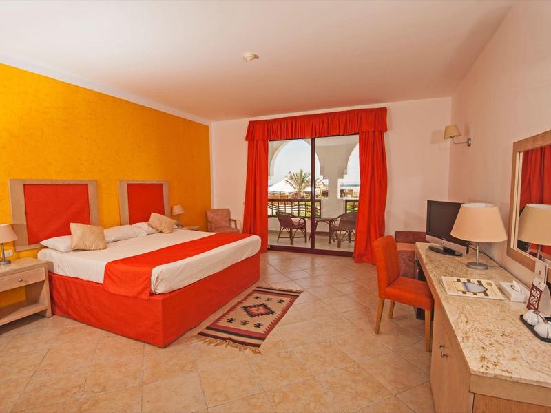 Chambre d'hôtel lumineuse avec lit double, accents orange et balcon donnant sur le jardin.