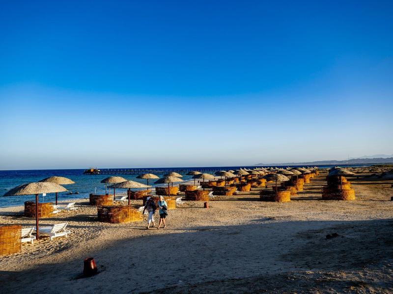 Plage avec de nombreuses huttes en paille et parasols sous un ciel bleu clair.