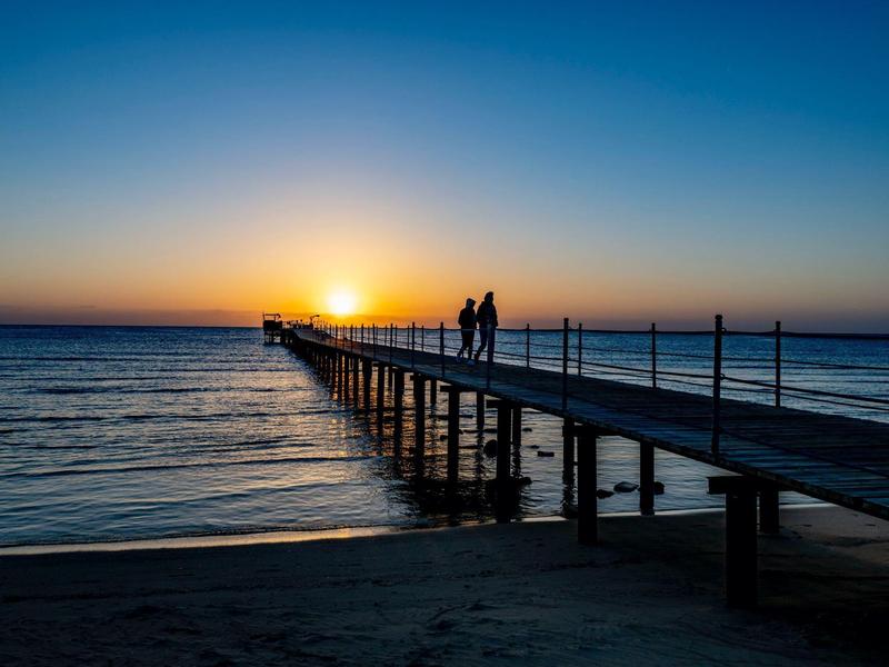 Longue jetée s'étendant dans la mer au coucher du soleil avec deux personnes dessus.