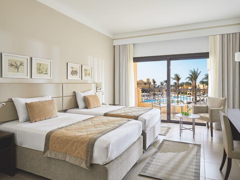Bright hotel room with two twin beds and a view of a pool and palm trees.