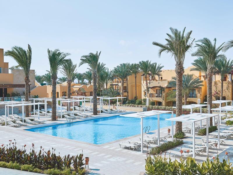 Modern hotel pool with lounge chairs and palm trees under clear sky.