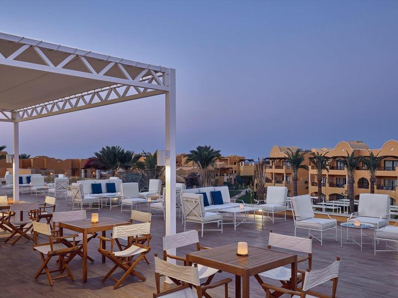 Modern outdoor restaurant with white furniture and view of buildings at dusk.