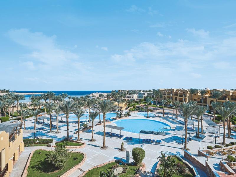Large resort pool area with palm trees and ocean view under a blue sky.