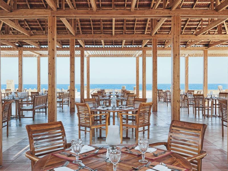 Offenes Strandrestaurant aus Holz mit Meerblick, Holztischen und Stühlen, gedeckt für Gäste.