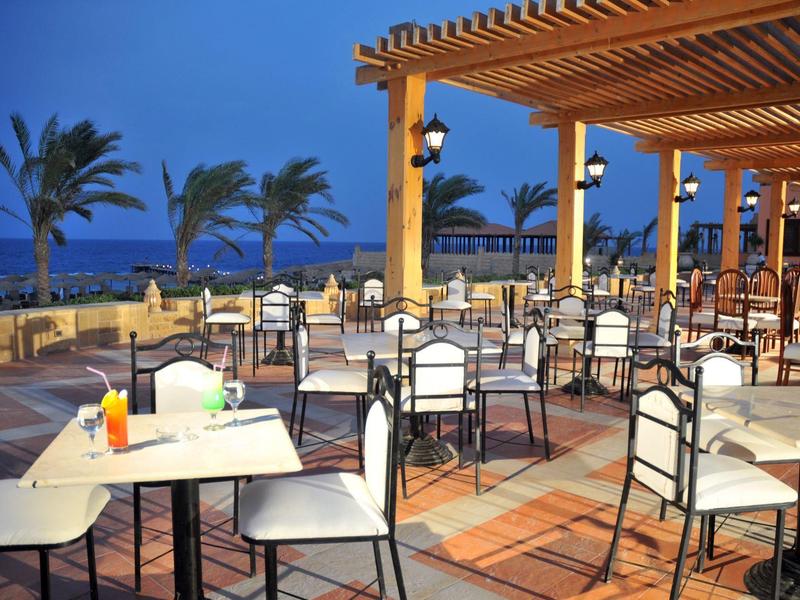 Freiluftrestaurant mit Tischen, Stühlen, Palmen und Blick auf das Meer bei Dämmerung.