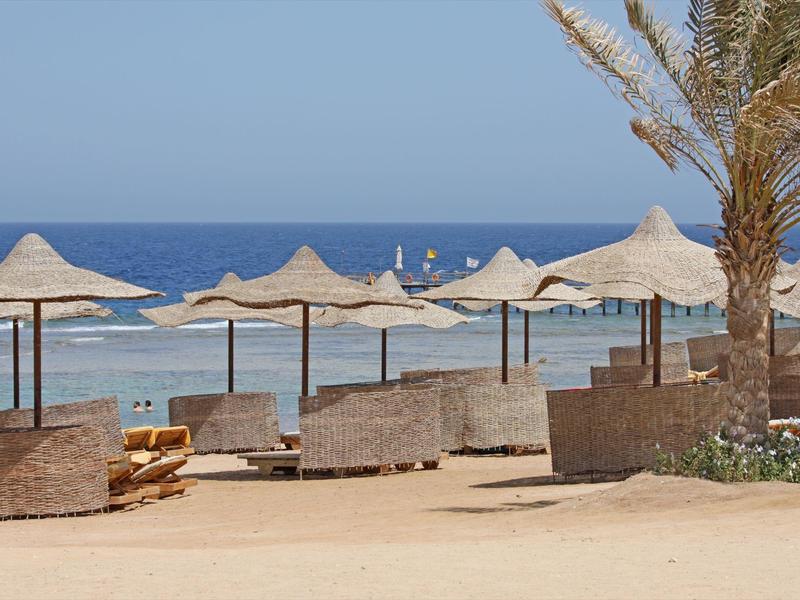 Beach with straw umbrellas and wooden lounge chairs near the ocean under a clear sky.