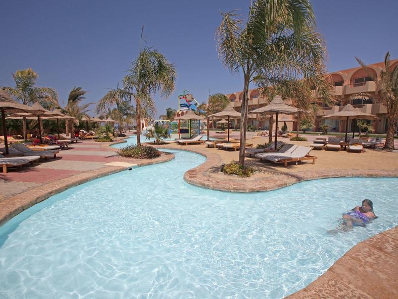 Outdoor swimming pool with sun loungers and umbrellas at a sunny resort.