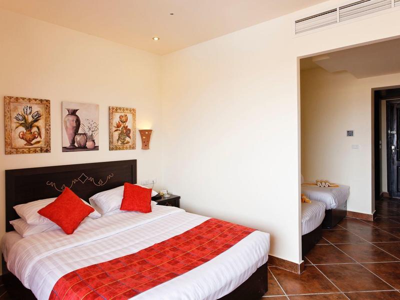 Hotel room with a double bed, red cushions, and a small adjacent room with a single bed.