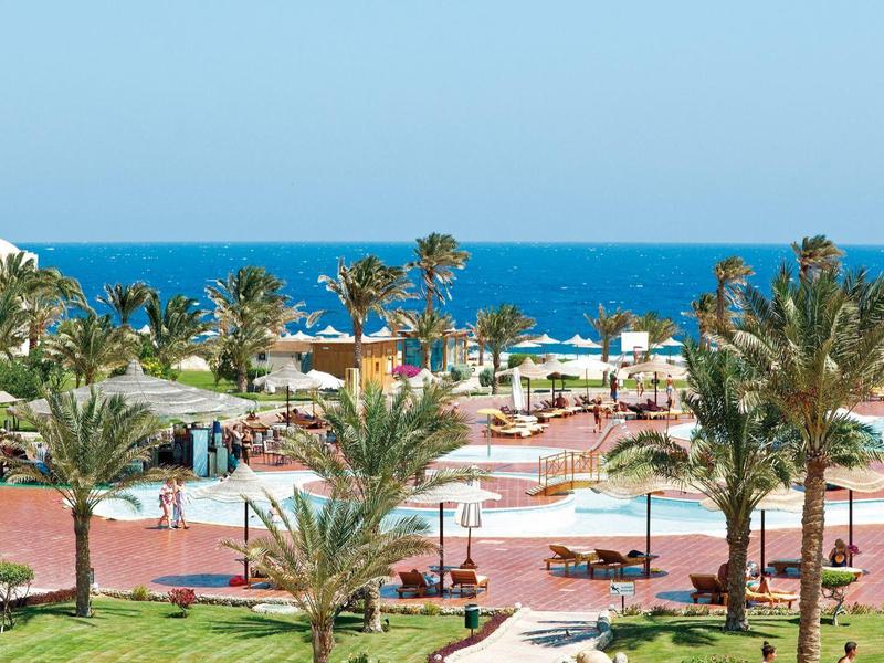 Hotel grounds with palm trees, walkways, and sea view under clear sky.