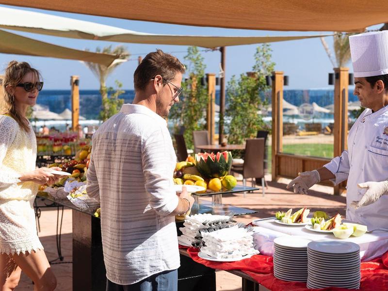 Guests enjoying an outdoor buffet at a beachside resort under a canopy.