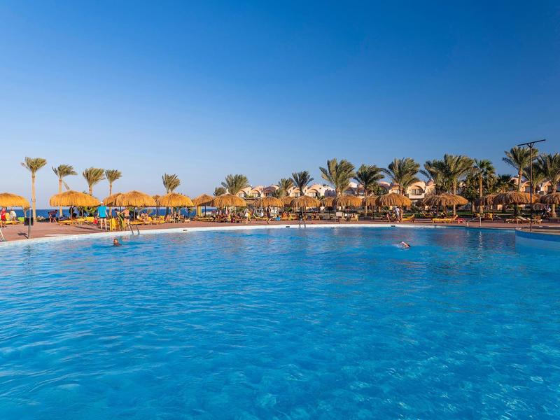 Clear blue pool with yellow sun umbrellas and palm trees under a bright sky