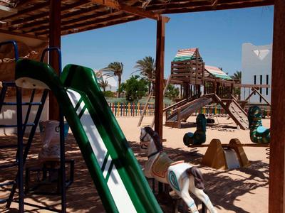 Área de juegos al aire libre con tobogán verde, figuras de animales y estructura bajo techo en hotel