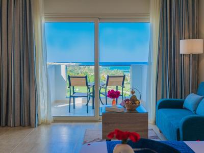 Balkon se stolem, židlemi a modrými žaluziemi s výhledem na zelenou krajinu.