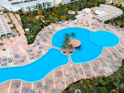 Großer, geschwungener Pool mit zwei Inseln, umgeben von Liegen und viel Grün in urbaner Umgebung.