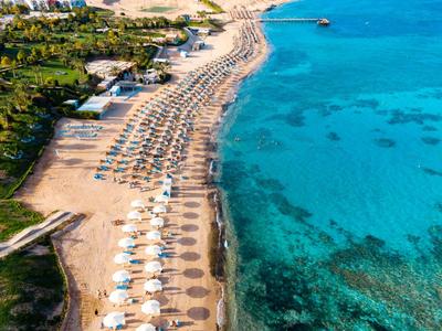 Letecký pohled na pláž s řadami slunečníků podél čisté modré vody.