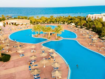 Grande piscina blu dell'hotel con ombrelloni e lettini, circondata da alberi e vista mare.