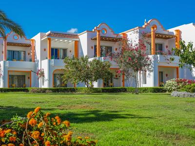 Hotel bianco con dettagli arancioni, circondato da prato verde e piante fiorite.
