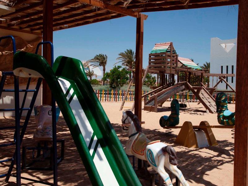 Área de juegos al aire libre con tobogán verde, figuras de animales y estructura bajo techo en hotel