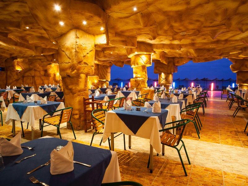 Restaurante al aire libre con diseño de cueva y mesas con manteles blancos y azules por la noche.