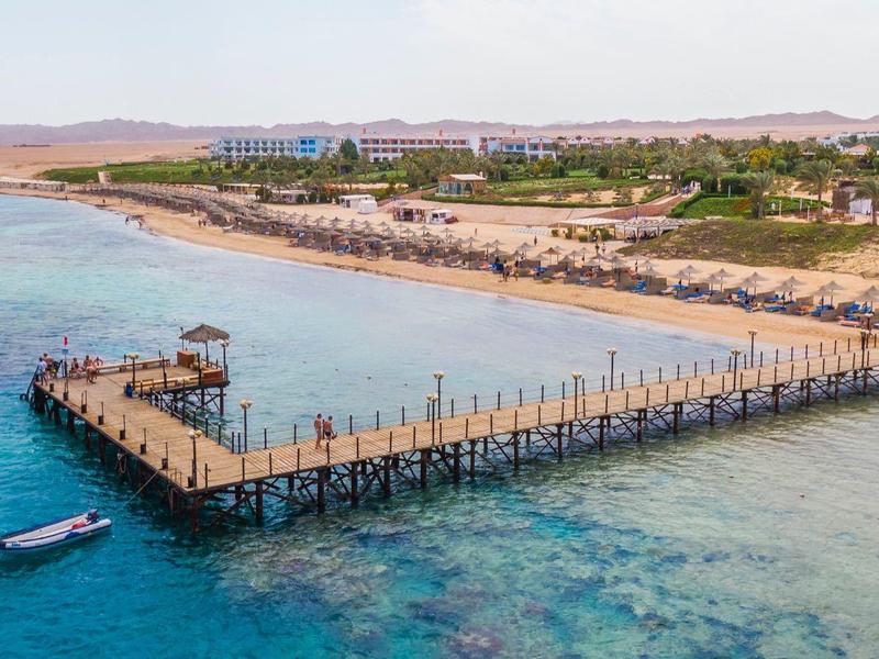 Largo muelle de madera con lugar para barco en mar turquesa claro junto a costa arenosa.