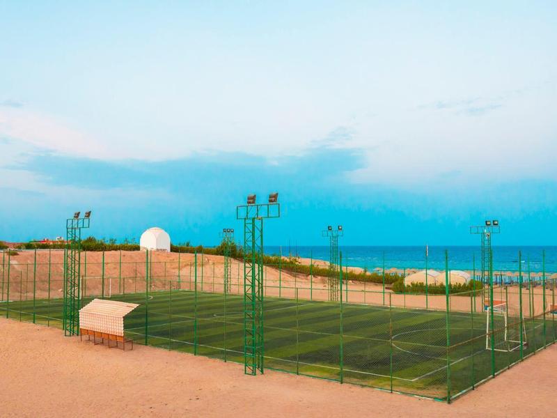 Cancha de tenis verde al aire libre con pista de tierra y cielo azul de fondo.