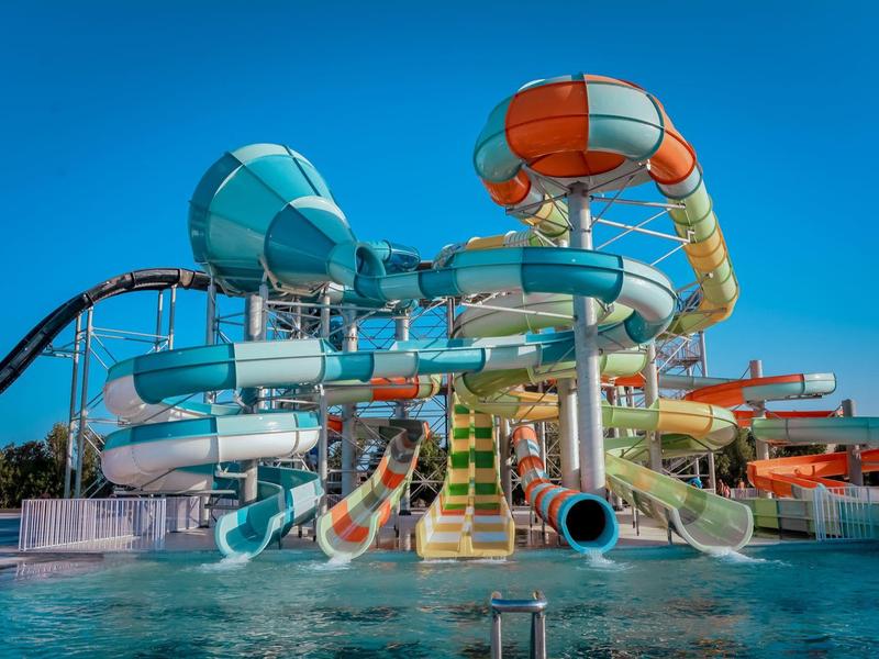 Toboganes de agua coloridos en un parque acuático sobre una piscina bajo un cielo despejado.