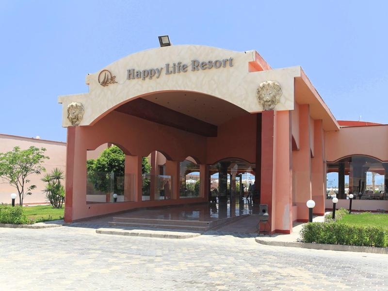 Eingangsbereich des Happy Life Resort mit roten Pfeilern und blauem Himmel.