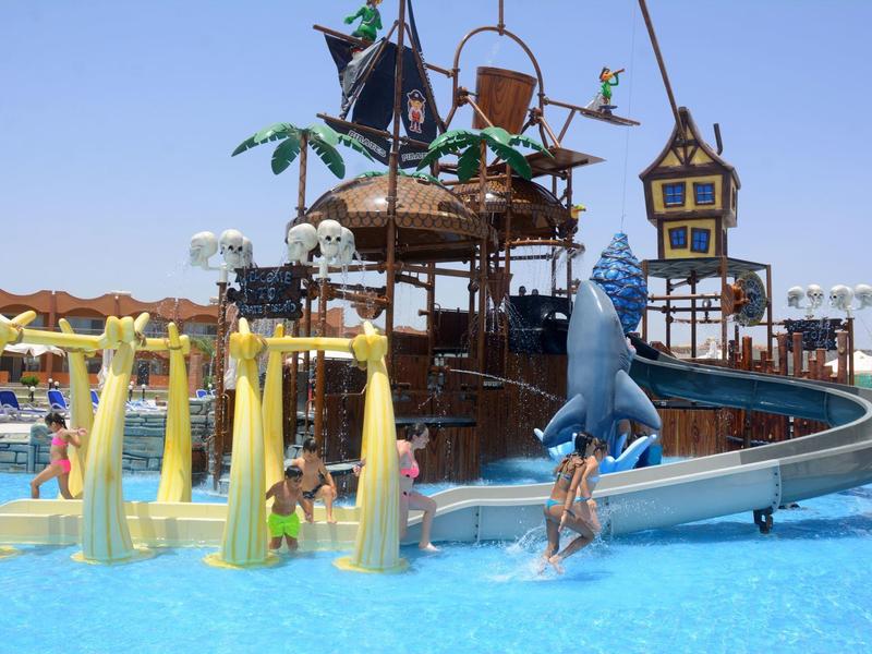 Wasserpark mit braunem Piratenschiff, blauer Rutsche und gelben Wasserspielen im klaren Pool.