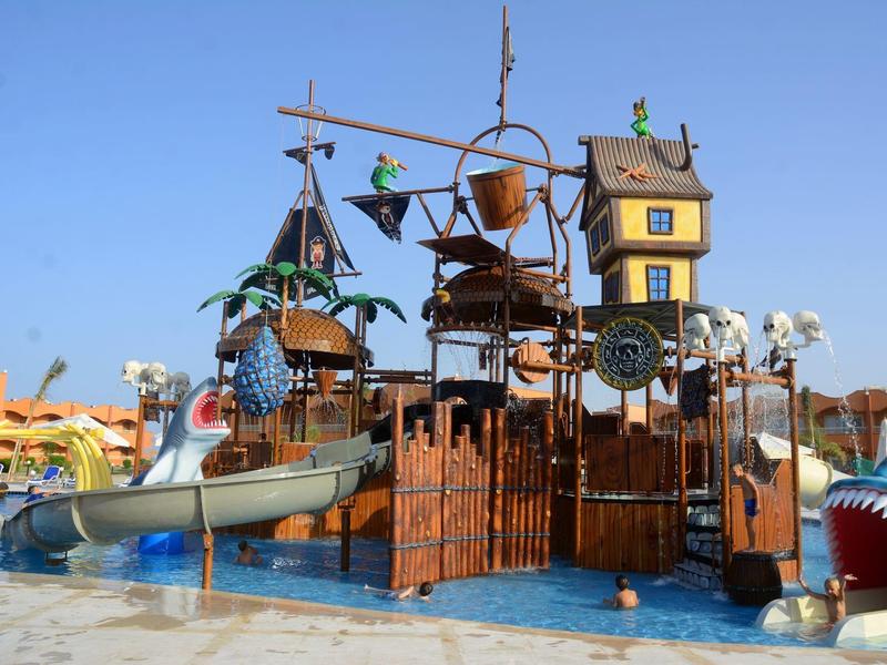 Buntes Wasserspielplatz mit Rutschen, Gondeln und Schiffsdekoration unter klarem Himmel.