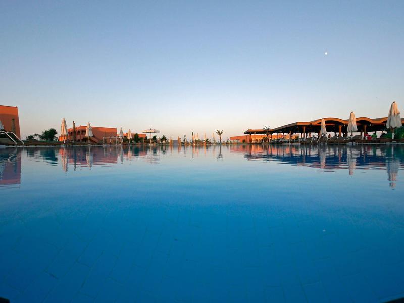 Großer Pool bei Sonnenuntergang mit klarblauem Himmel und Liegestühlen auf beiden Seiten.