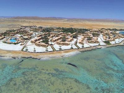 Vista aérea de una isla con instalaciones hoteleras rodeada de mar turquesa y arrecifes de coral.
