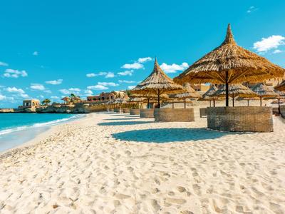 Plage de sable avec parasols en paille et un hôtel en arrière-plan sous un ciel bleu