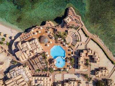 Vue aérienne d'un complexe avec piscine au bord de la côte et eau de mer turquoise.