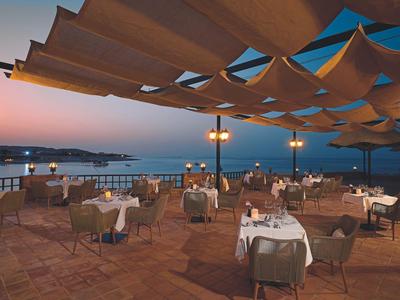 Terrasse élégamment aménagée avec tables et chaises au bord de la mer au coucher du soleil.