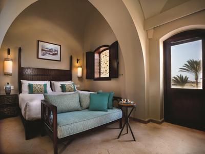 Elegante habitación de hotel con cama con dosel, sofá y vista a una palmera por la ventana.