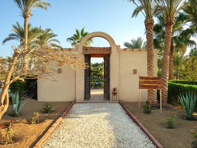 Entrada a un jardín de hotel con palmeras y un camino de piedras blancas.