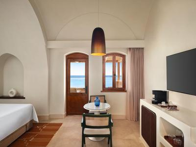 Habitación de hotel luminosa y moderna con ventana grande, vista al mar y diseño minimalista.