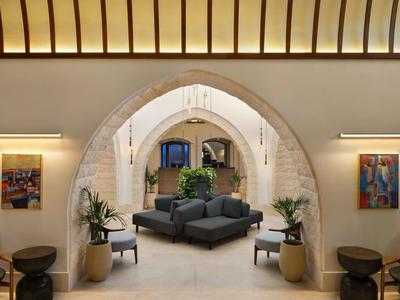 Salón luminoso de hotel con sofás grises, plantas y arcos de estilo mediterráneo.