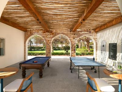 Espace de loisirs couvert avec billard et table de ping-pong, entouré d'arcades avec vue sur le jardin.