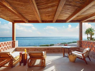 Terrasse couverte avec plafond en bois, mobilier et vue dégagée sur la mer sous un ciel bleu.