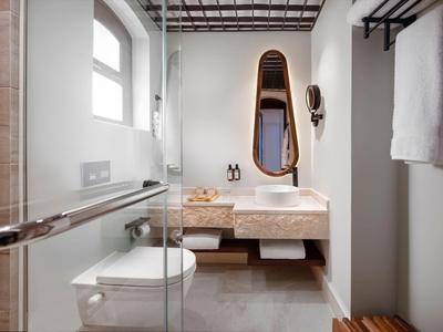 Baño moderno con ducha, inodoro, lavabo y grandes ventanas en tonos neutros.