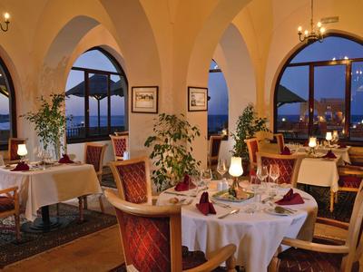 Restaurante elegante con mesas vestidas y grandes ventanales arqueados con vista al agua.