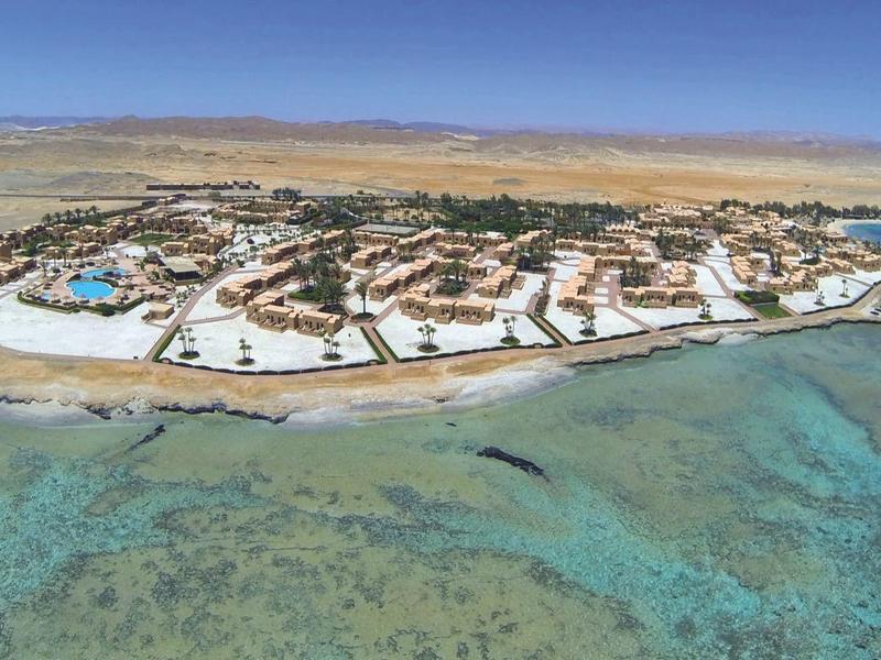 Vista aérea de una isla con instalaciones hoteleras rodeada de mar turquesa y arrecifes de coral.